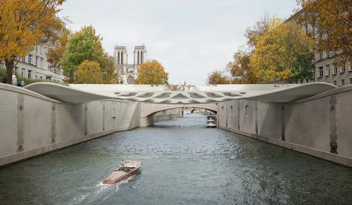 The 3D-printed Diamanti Bridge in Paris, spanning the river with curved forms and hollow surfaces created through parametric design, complementing the surroundings with autumn trees and historic buildings.